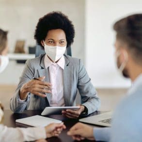 Bank manager with face mask using touchpad while talking to her clients on a meeting in the office.