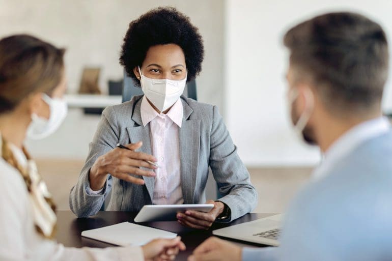 Bank manager with face mask using touchpad while talking to her clients on a meeting in the office.