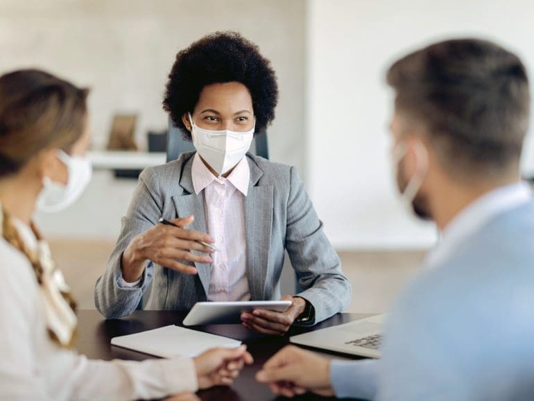 Bank manager with face mask using touchpad while talking to her clients on a meeting in the office.