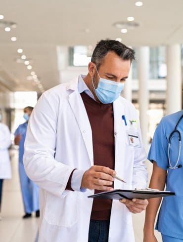 General practitioner and young nurse wearing surgical face masks.