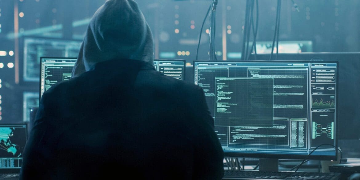 Dangerous Hooded Hacker Breaks into Government Data Servers and Infects Their System with a Virus. His Hideout Place has Dark Atmosphere, Multiple Displays, Cables Everywhere.