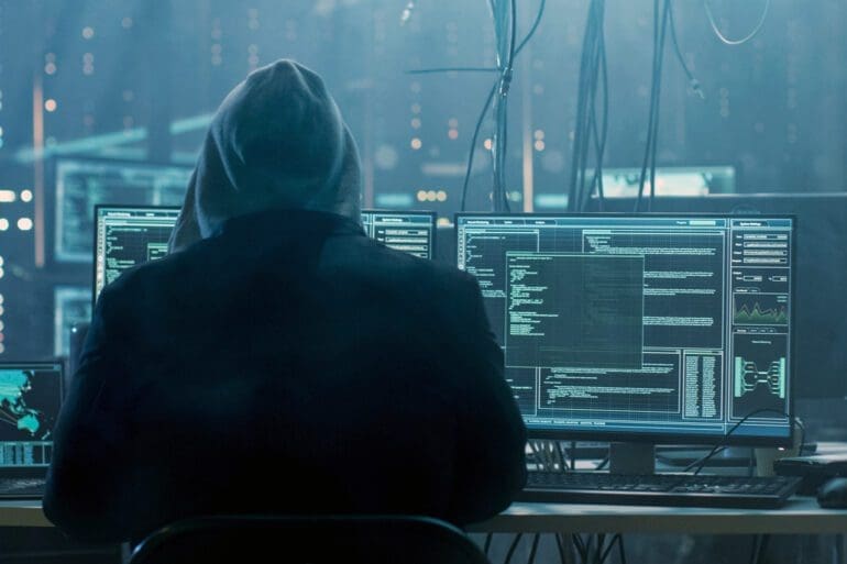 Dangerous Hooded Hacker Breaks into Government Data Servers and Infects Their System with a Virus. His Hideout Place has Dark Atmosphere, Multiple Displays, Cables Everywhere.