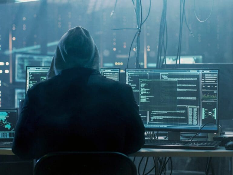 Dangerous Hooded Hacker Breaks into Government Data Servers and Infects Their System with a Virus. His Hideout Place has Dark Atmosphere, Multiple Displays, Cables Everywhere.