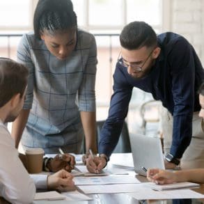 Focused multiracial corporate business team people brainstorm on marketing plan financial report gather at office table meeting, diverse serious colleagues group discuss paperwork engaged in teamwork