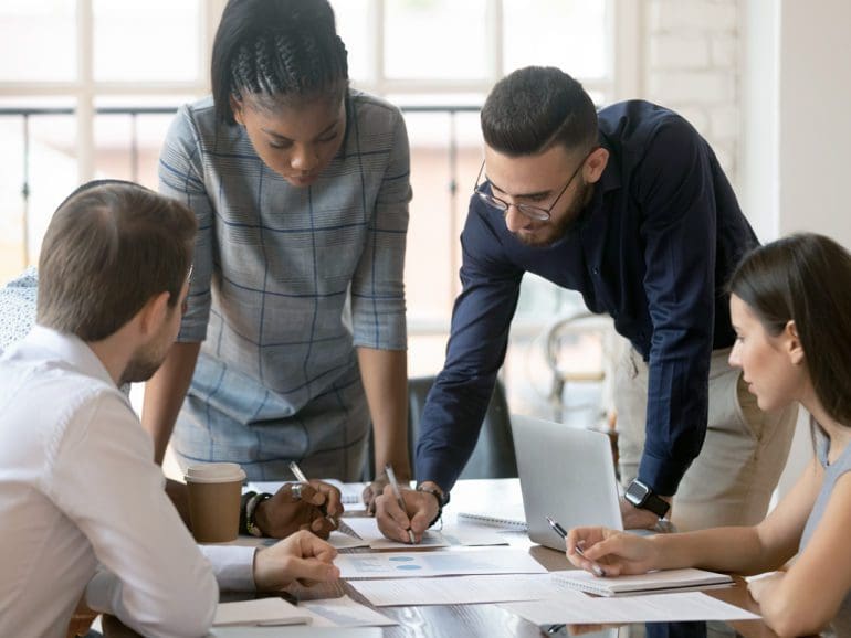 Focused multiracial corporate business team people brainstorm on marketing plan financial report gather at office table meeting, diverse serious colleagues group discuss paperwork engaged in teamwork