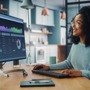 Latina Female Specialist Working on Desktop Computer at Home Living Room while Sitting at a Table. Freelance Female is Doing Market Analysis and Creates Report with Charts for Clients and Employer.