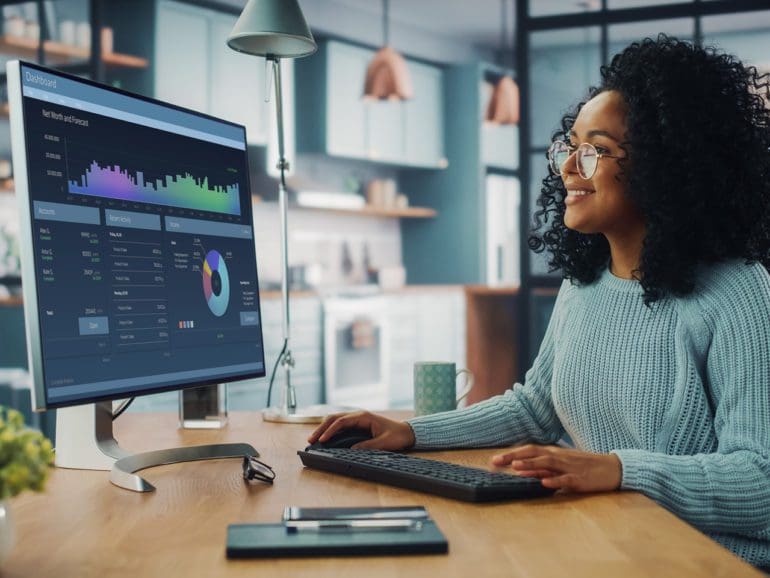 Latina Female Specialist Working on Desktop Computer at Home Living Room while Sitting at a Table. Freelance Female is Doing Market Analysis and Creates Report with Charts for Clients and Employer.