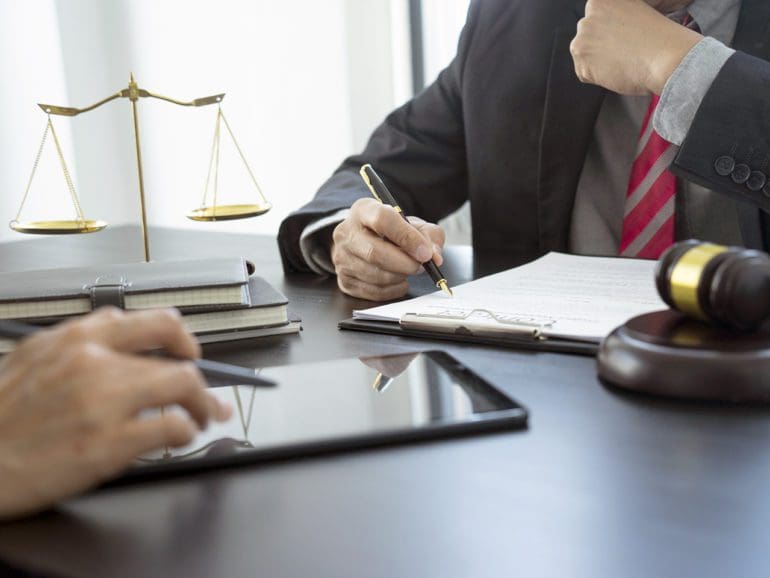 The lawyer is reviewing the draft of legal documents or contracts for clients near the staff or the client is checking work together by using a tablet.