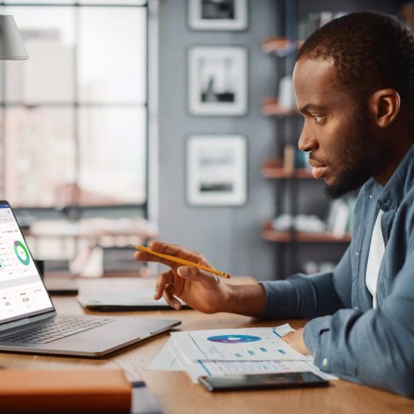 Handsome Black African American Specialist Working on Laptop Computer in Creative Home Living Room. Freelance Male is Doing Market Analysis and Creates Report with Charts for Clients and Employer.