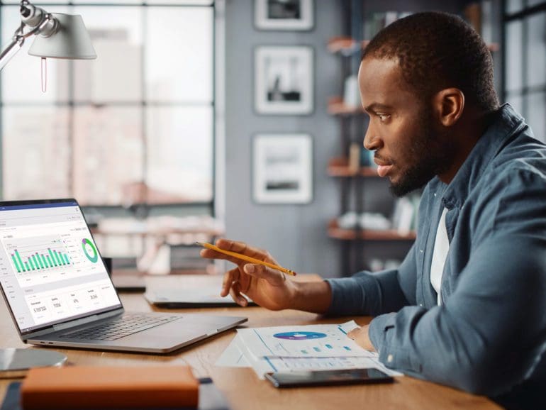 Handsome Black African American Specialist Working on Laptop Computer in Creative Home Living Room. Freelance Male is Doing Market Analysis and Creates Report with Charts for Clients and Employer.