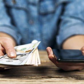 Woman holds dollars and phone in her hands. Online money transfer.