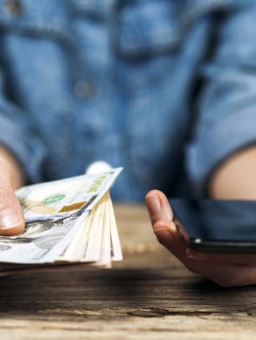 Woman holds dollars and phone in her hands. Online money transfer.
