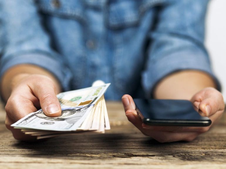 Woman holds dollars and phone in her hands. Online money transfer.