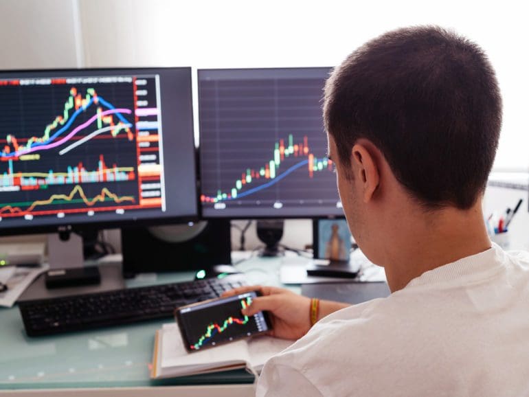 Busy working day at home. Side view of successful young trader in casual wear working with charts and market reports on computer screens in his home.