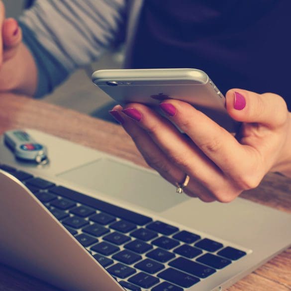 Woman holding smart phone and working on laptop