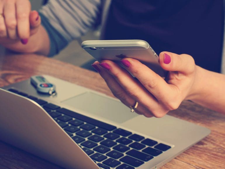 Woman holding smart phone and working on laptop