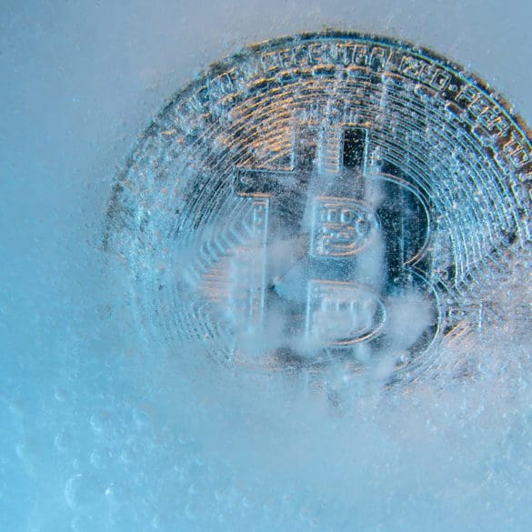 Silver Bitcoin, bit coin online digital currency frozen in the blue ice. Concept of block chain, crypto market crash. Frozen crypto money, depreciation