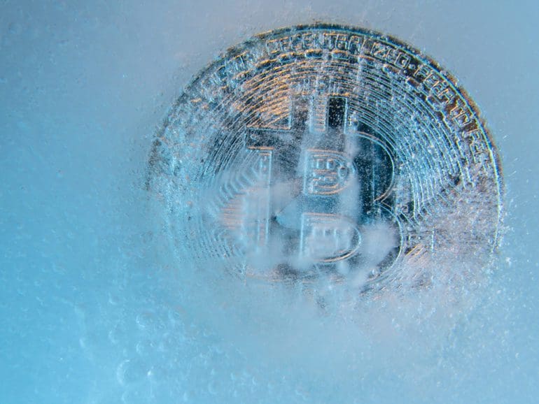 Silver Bitcoin, bit coin online digital currency frozen in the blue ice. Concept of block chain, crypto market crash. Frozen crypto money, depreciation