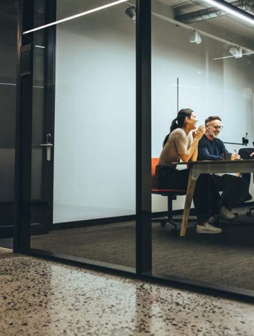 Business colleagues having a meeting in a transparent boardroom. Group of happy business professionals having a discussion during a briefing. Diverse businesspeople collaborating on a new project.