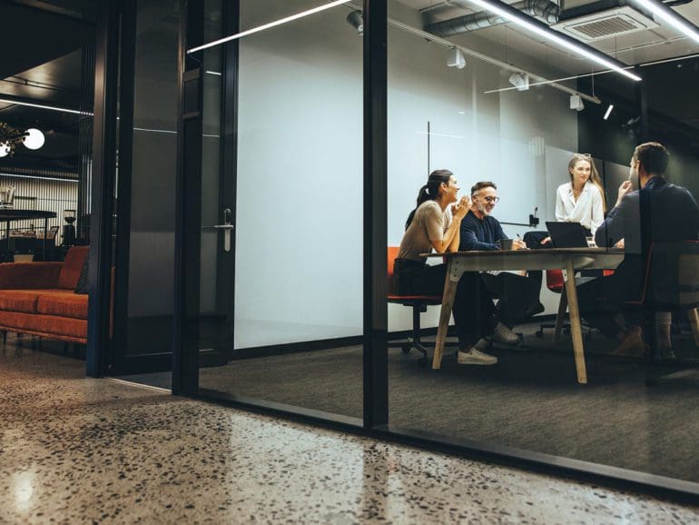 Business colleagues having a meeting in a transparent boardroom. Group of happy business professionals having a discussion during a briefing. Diverse businesspeople collaborating on a new project.