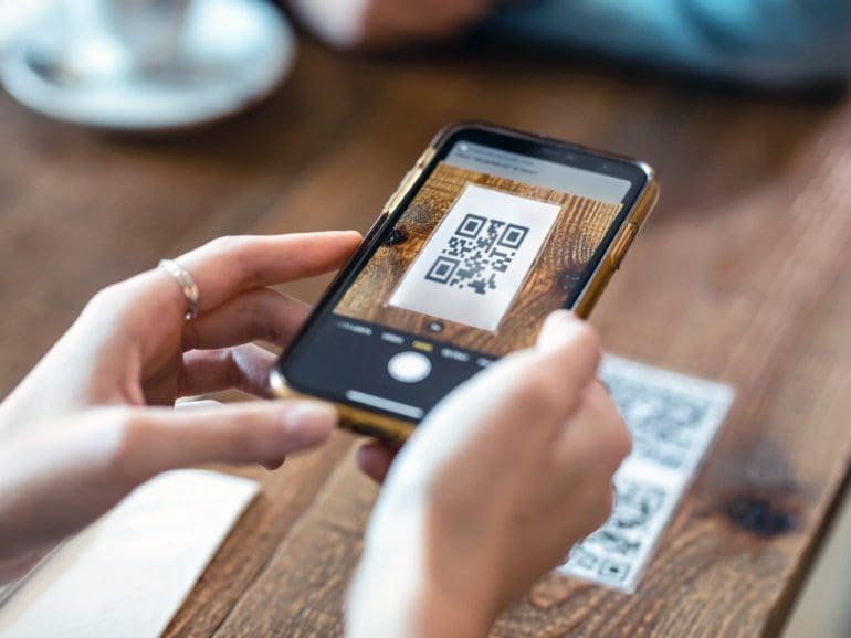 Close up of young woman hands using the smart phone to scan the qr code to select food menu in the restaurant.