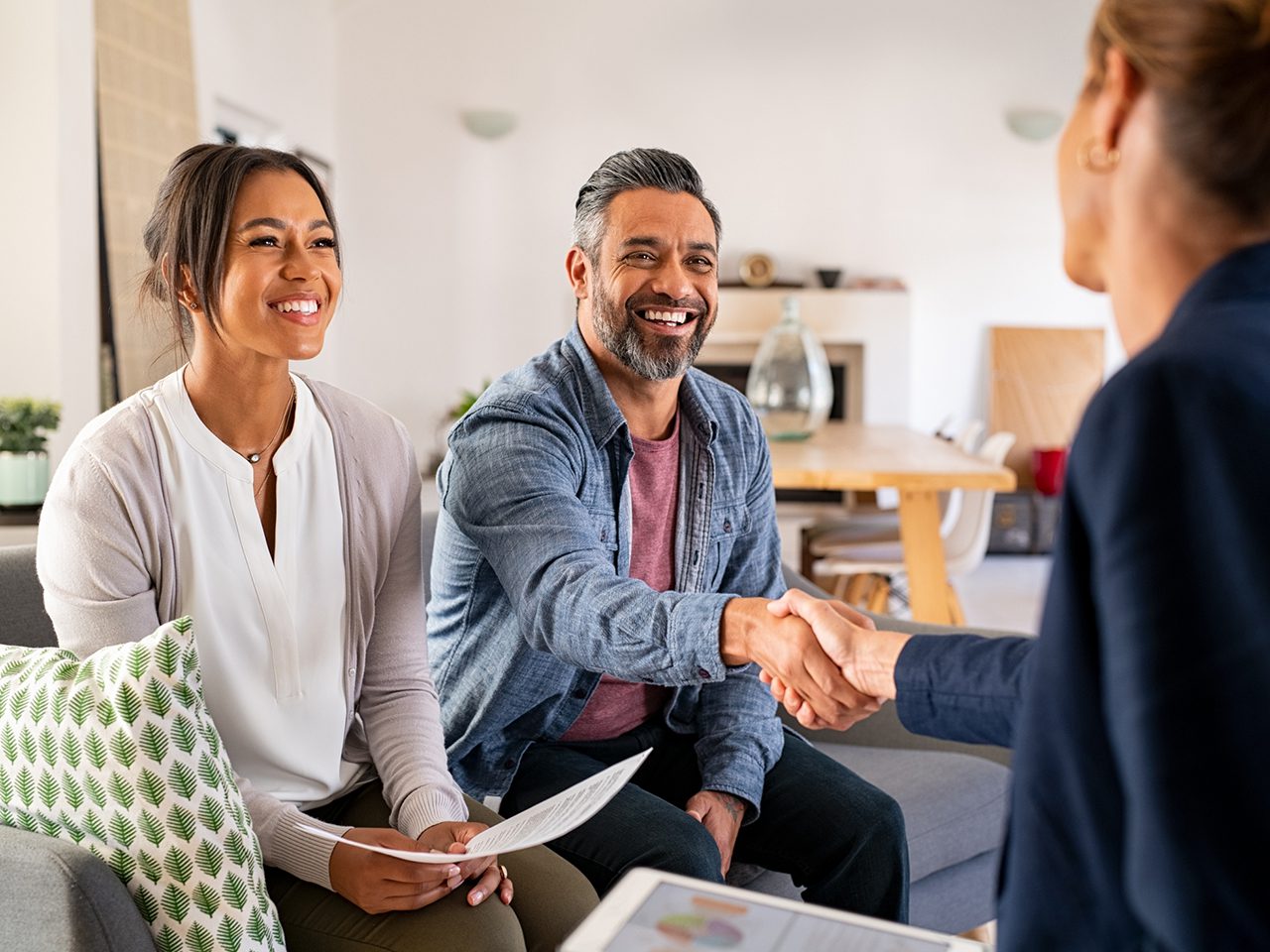 Mature indian man shaking hands with financial advisor at home. Happy smiling couple greeting broker with handshake at home. Multiethnic mid adult man and hispanic woman sealing a contract.