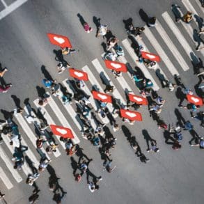 Different people at a pedestrian crossing with social heart icons and likes in the city. People at a zebra pedestrian crossing - a lot of pedestrians in an overcrowded city on a sunny day.