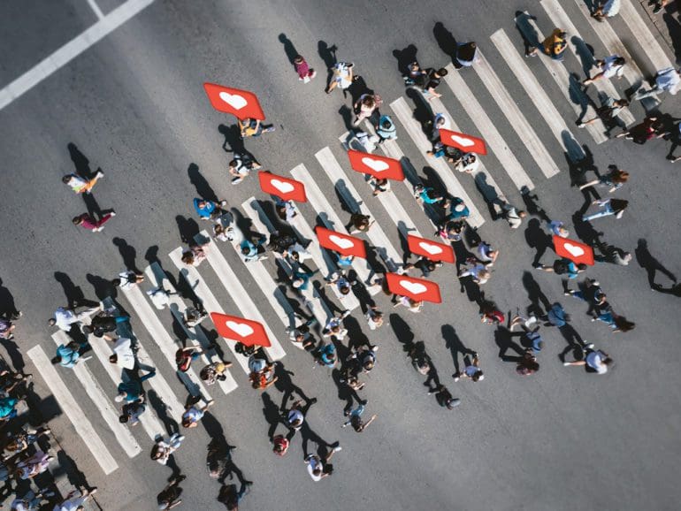 Different people at a pedestrian crossing with social heart icons and likes in the city. People at a zebra pedestrian crossing - a lot of pedestrians in an overcrowded city on a sunny day.