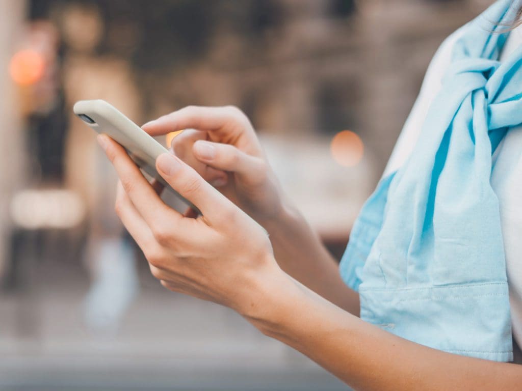 Close-up photo of female hands with smartphone. Young woman typing on a mobile phone on a sunny street