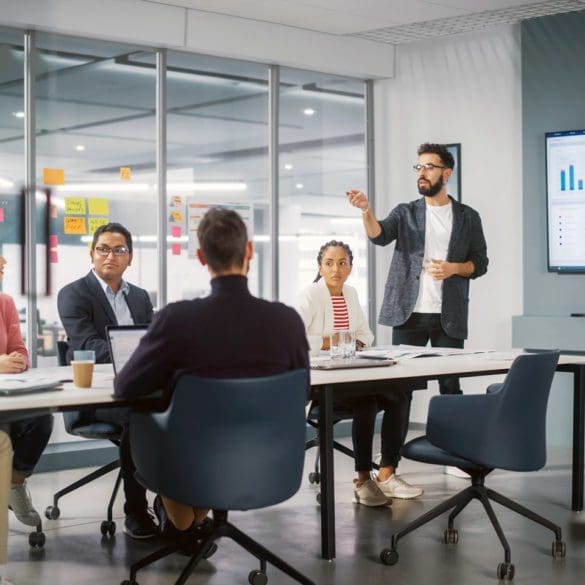 Diverse Modern Office: Businessman Leads Business Meeting with Managers, Talks, uses Presentation TV with Statistics, Infographics. Digital Entrepreneurs Work on e-Commerce Project.