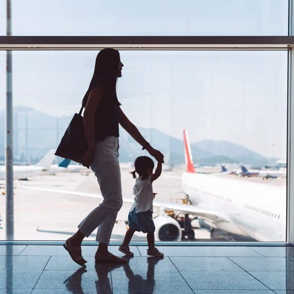 Silhouette of joyful young Asian mother holding hands of cute little daughter looking at airplane through window at the airport while waiting for departure