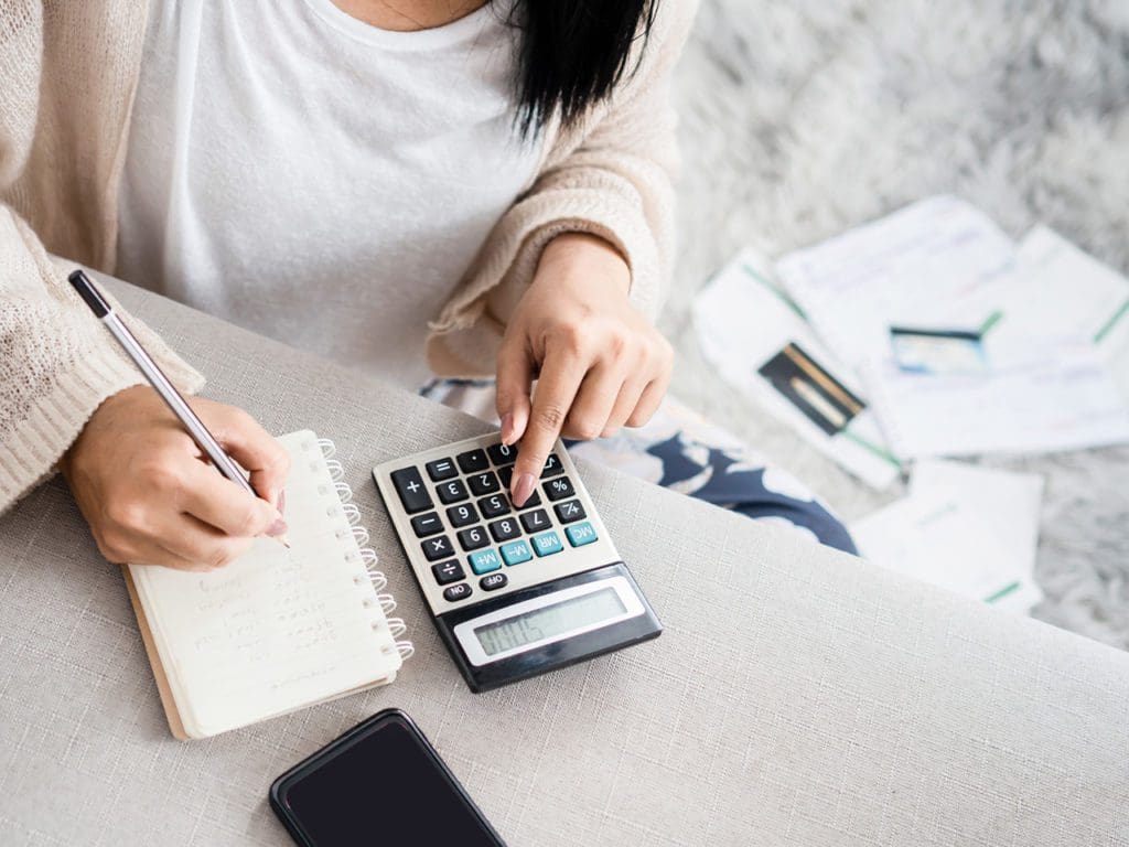 woman writing a list of debt on notebook calculating her expenses with calculator with many invoices , female hand doing accounting