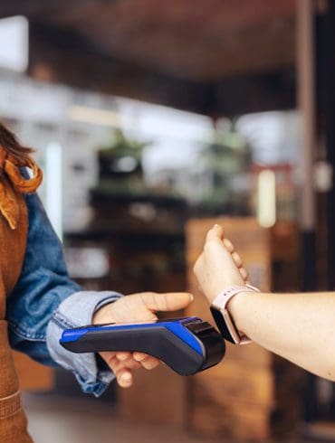 Happy customer scanning her smartwatch on a credit card machine to pay her bill in a cafe. Cheerful woman doing a cashless and contactless transaction using NFC technology.