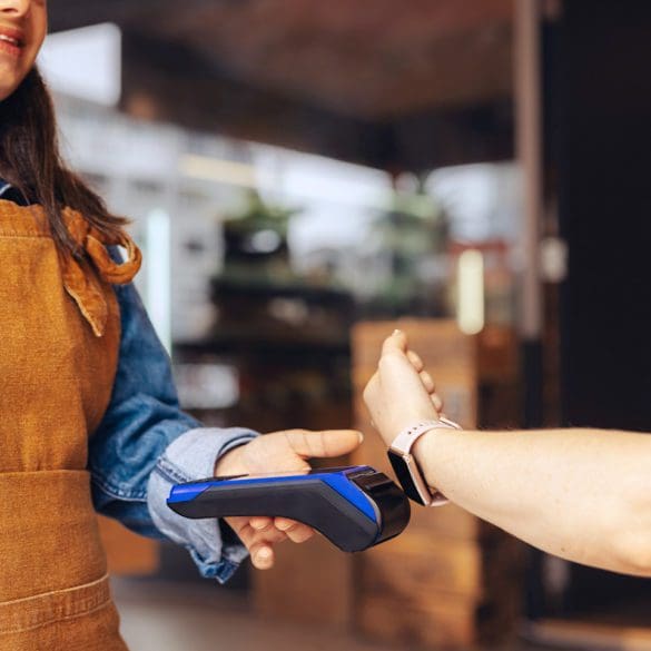 Happy customer scanning her smartwatch on a credit card machine to pay her bill in a cafe. Cheerful woman doing a cashless and contactless transaction using NFC technology.