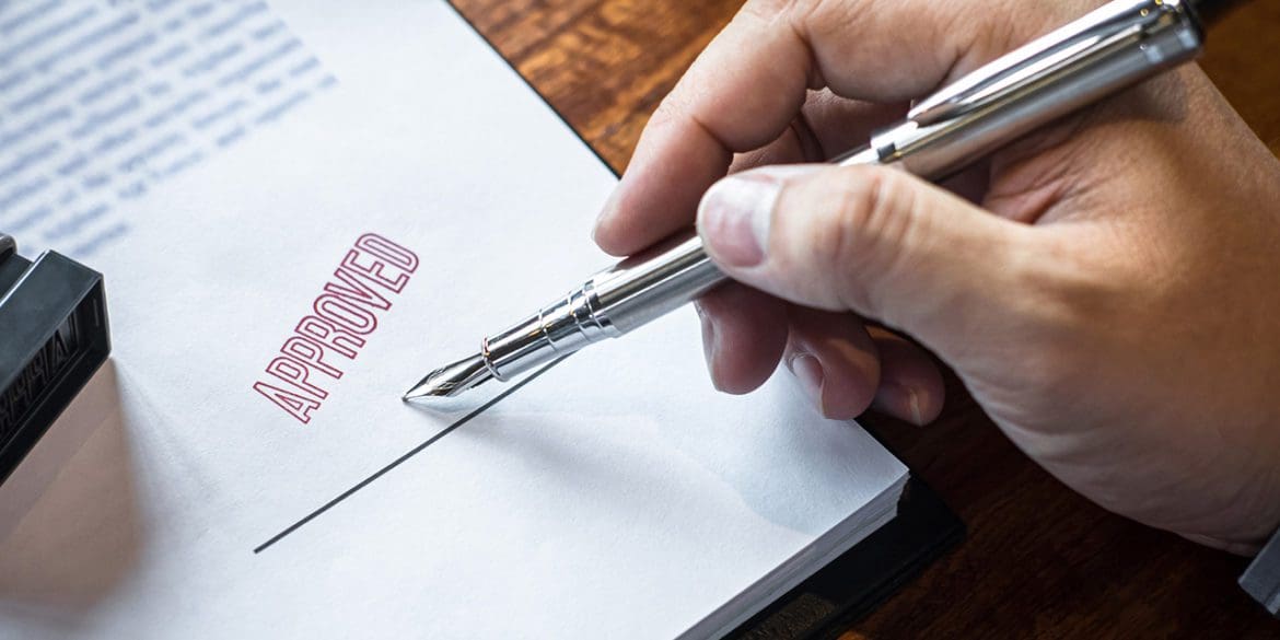 Close up hands of businessman signing and stamp on paper document to approve business investment contract agreement.