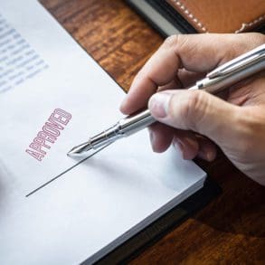 Close up hands of businessman signing and stamp on paper document to approve business investment contract agreement.