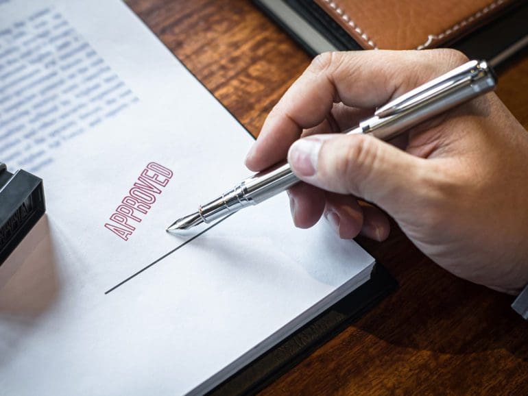 Close up hands of businessman signing and stamp on paper document to approve business investment contract agreement.