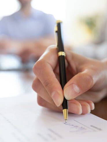 Close up young woman putting signature on banking loan document in office. Successful businesswoman signing contract or purchase document with partners at meeting after negotiations and making edits.