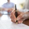 Close up young woman putting signature on banking loan document in office. Successful businesswoman signing contract or purchase document with partners at meeting after negotiations and making edits.