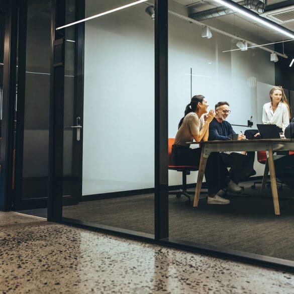 Business colleagues having a meeting in a transparent boardroom. Group of happy business professionals having a discussion during a briefing. Diverse businesspeople collaborating on a new project.