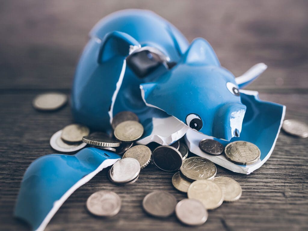 closeup of shattered broken piggy bank with coins on rustic wooden table