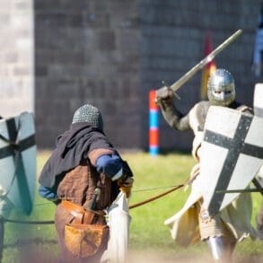 Located in Caboolture, the Abbey Medieval festival runs for a week and brings together lovers of all things old world. This image depicts several gentlemen dressed as knights in armor preparing retaliation to protect their king (and the castle you can see in the photo) during a battle in the LARP ring. The LARP battle take place in the large arena set upright in the heart of the festival. You can see the archer bracing to take his shot and the oncoming attack raising their shields in preparation. In this Image he is loading his bow with an arrow. This photo was taken at the festival on the 14th of July 2019 held at the Abbeystowe Museum.