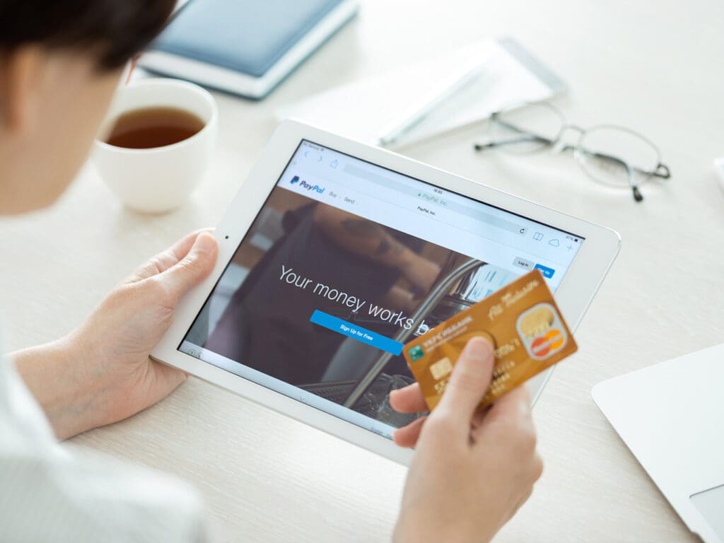 Kiev, Ukraine - June 27, 2014: Person with credit card in hand looking on a brand new Apple iPad Air with Paypal website on a screen. Paypal is the worldwide e-commerce business service allowing payments and money transfers via internet, founded in June, 1998.