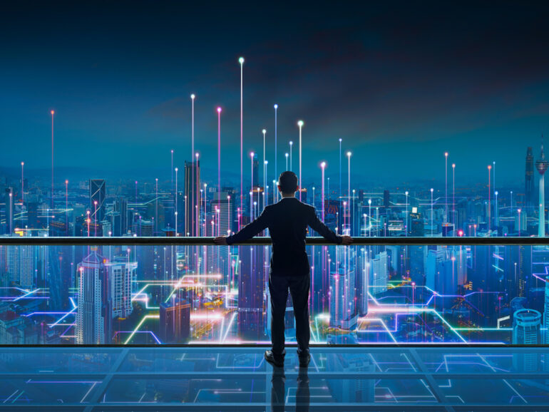 Businessman standing at transparent glass floor on rooftop with night Smart city panoramic view. Business success with smart technology concept